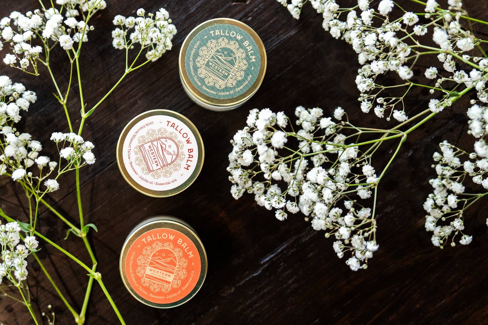 An assortment of Western Provisions tallow balm on a table surrounded by flowers